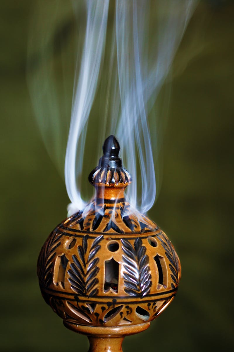 Elegant ceramic incense burner with intricate design and smoke rising against a green background.